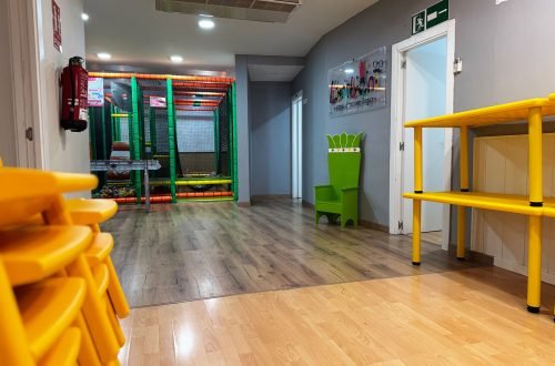 Interior de sala para cumpleaños y fiestas infantiles en Gavà con sillas apiladas, mesas amarillas, trono infantil verde y zona de juegos con bolas.